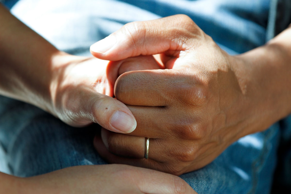 Caring hands holding a patient's hand in a comforting gesture.